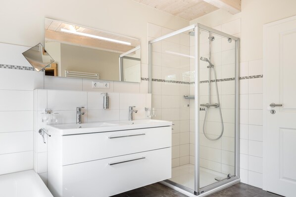 Une salle de bain moderne avec une douche à l’italienne, un meuble-lavabo blanc doté de deux tiroirs et un grand miroir au-dessus du lavabo.