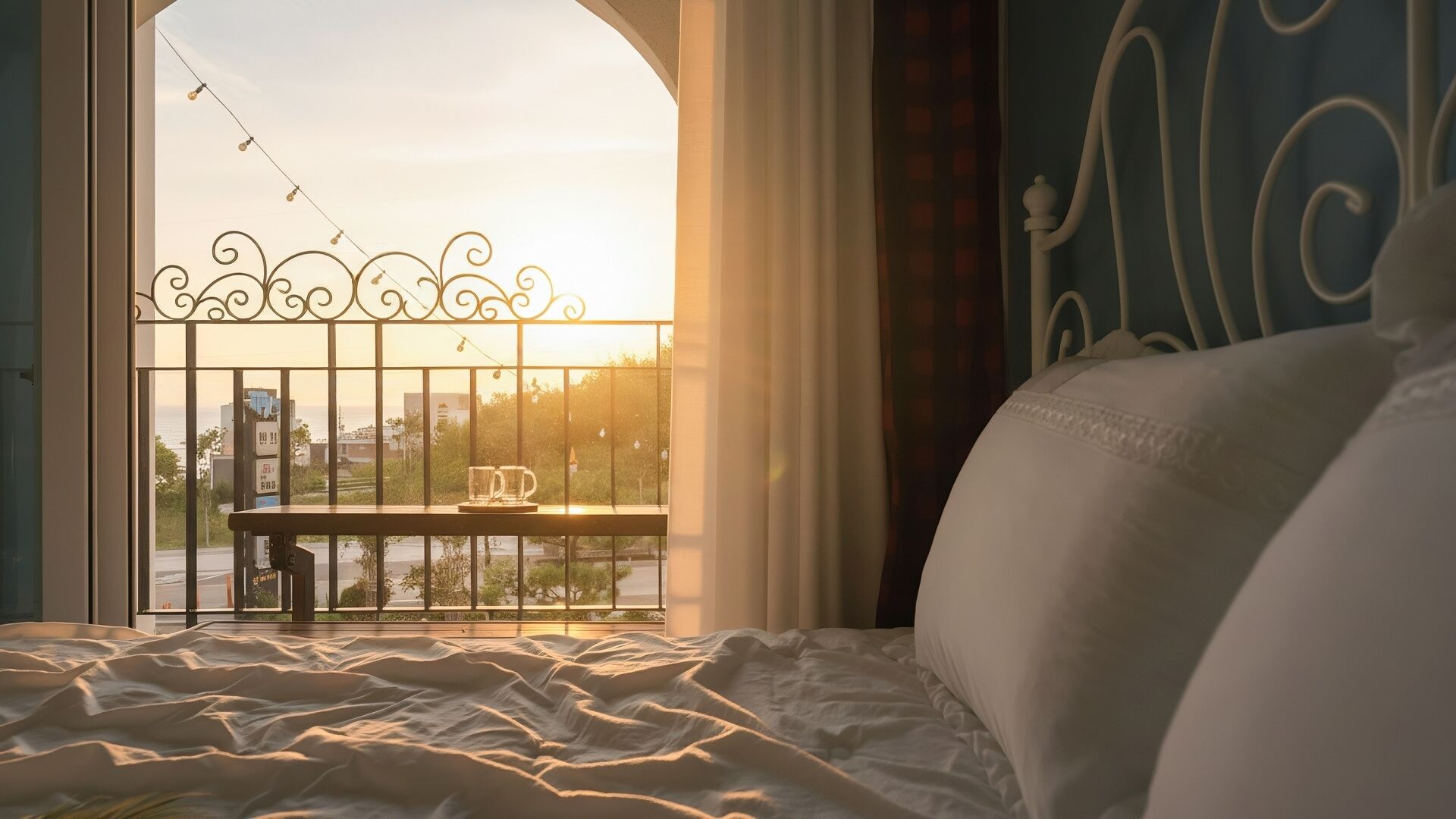 A bedroom with a view of a cityscape through a window with a decorative metal railing.