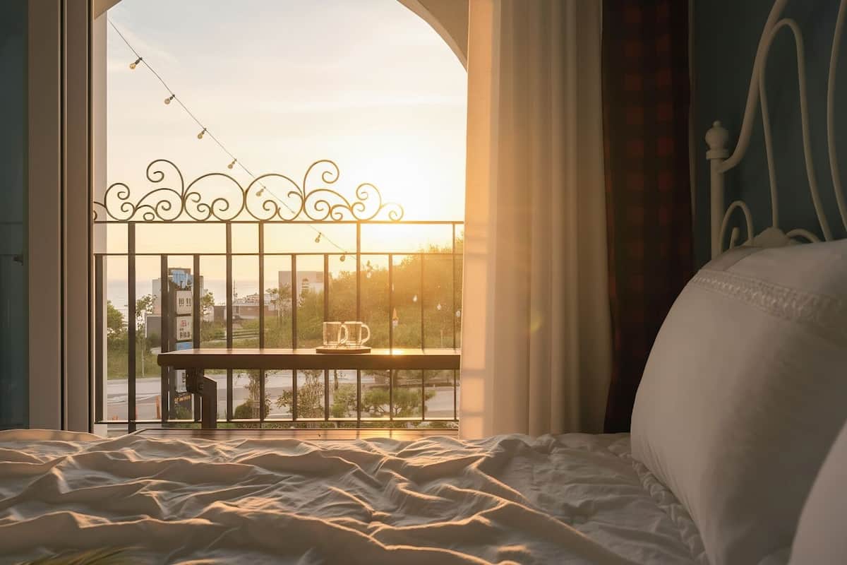 A bedroom with a view of a cityscape through a window with a decorative metal railing.