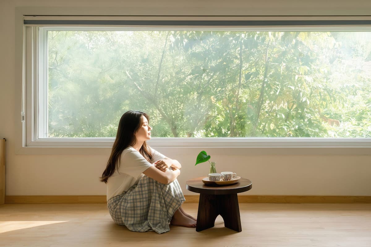 A room with a large window, a small wooden table with a cup and saucer, and a potted plant.