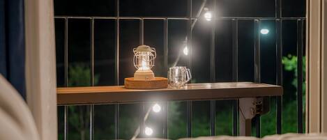 A window with a decorative metal grille, a white lamp, and a clear glass mug on a wooden ledge.