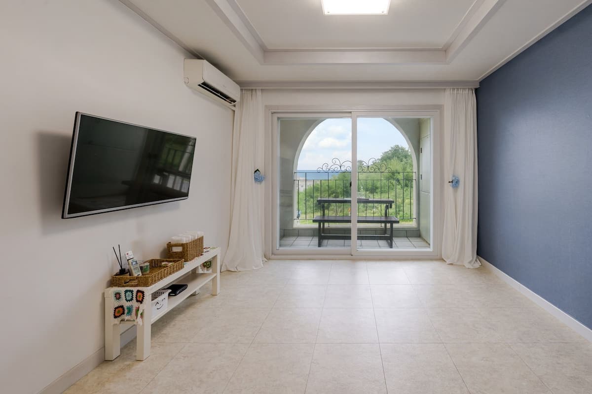 A modern room with a flat-screen TV mounted on the wall, a small table with baskets, and a bench by a sliding glass door leading to an outdoor area.