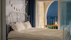 A bedroom with a white metal bed frame, white bedding, a wall-mounted heart decoration, and a view of the night sky through an arched window. - Samcheok Sea Road Pension (Samcheok)