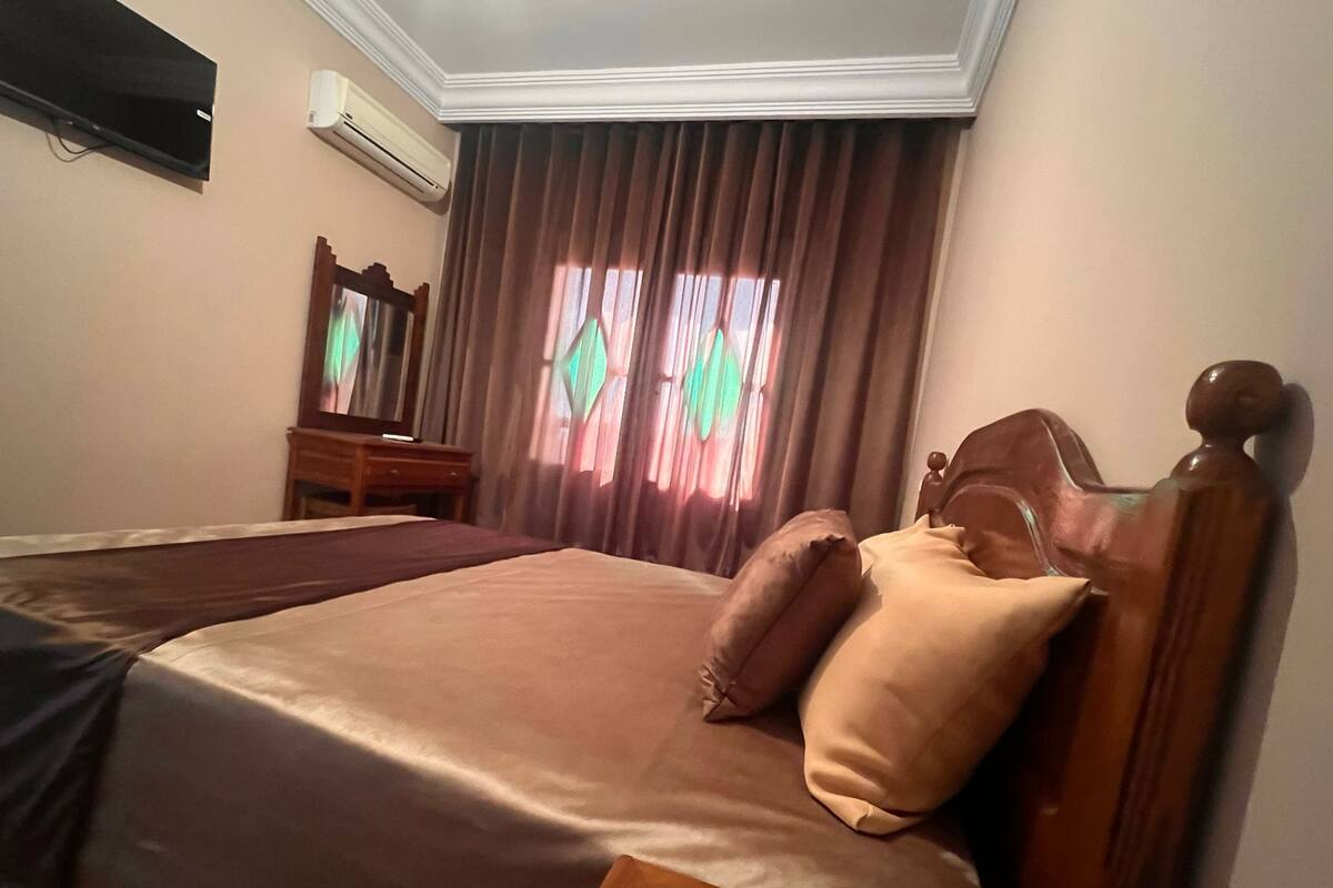 A neatly made bed with a wooden headboard, a wooden nightstand, a dresser, and a mirror.