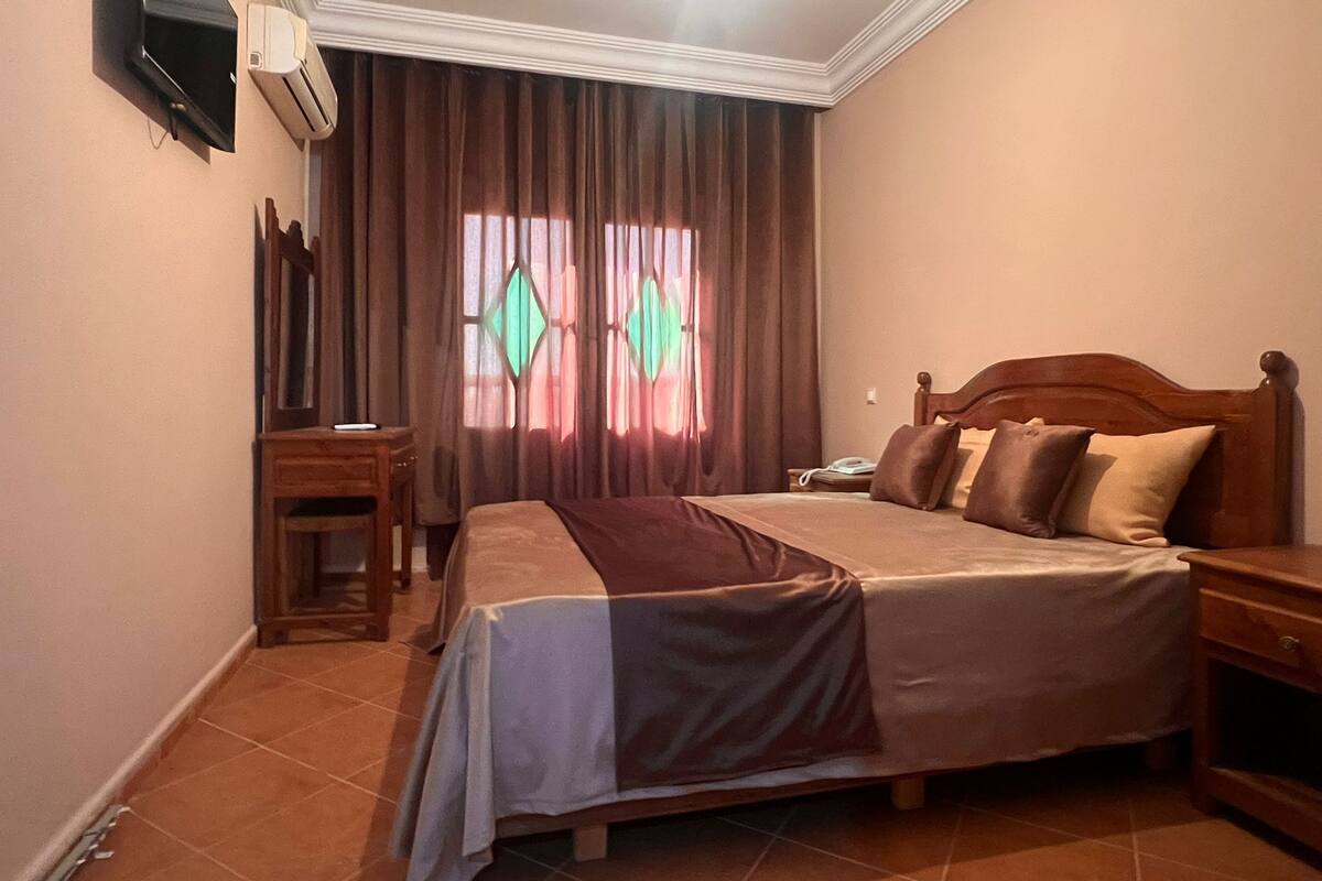 A hotel room with a bed, bedside table, and a TV mounted on the wall.