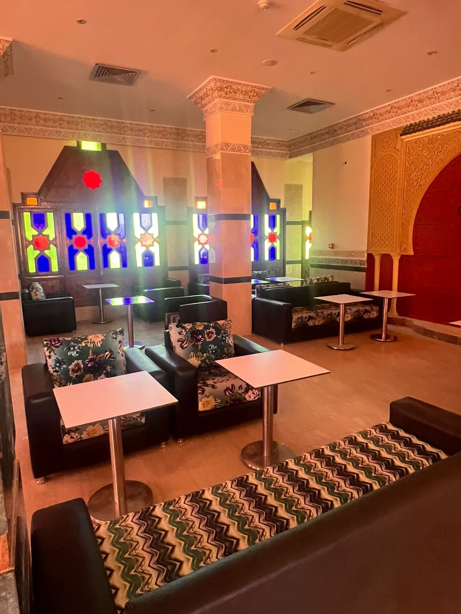 A hotel lobby with seating areas, a reception desk, and decorative stained glass windows.