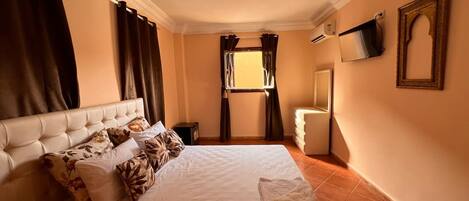 A hotel room with a large bed, a bedside table, a TV mounted on the wall, and a window with curtains.