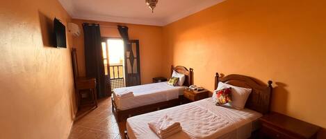 A room with two single beds, a wooden nightstand, a small table, and a ceiling light fixture.