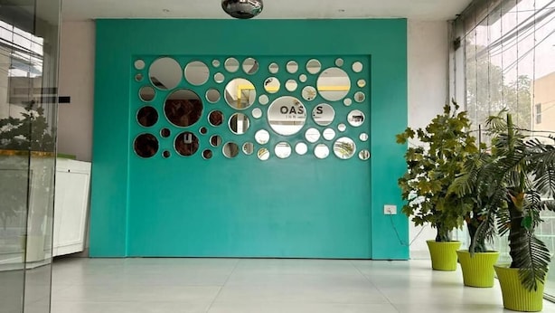 Un mur de couleur turquoise orné de miroirs ronds, avec les lettres « OAS » et « S » au centre. Des plantes en pot sont disposées sur le côté droit.