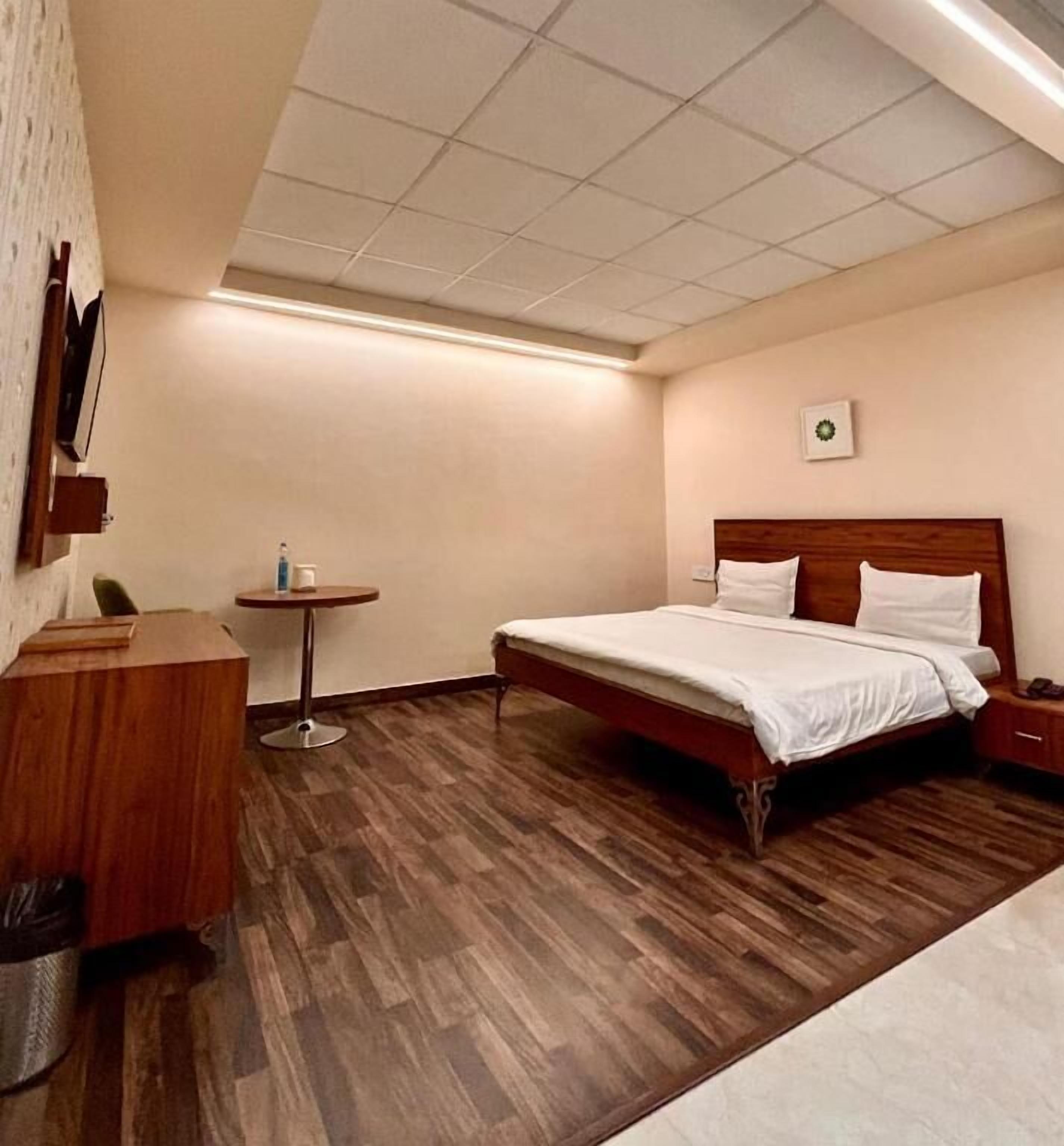 A hotel room with a wooden bed, a small round table, and a trash bin.