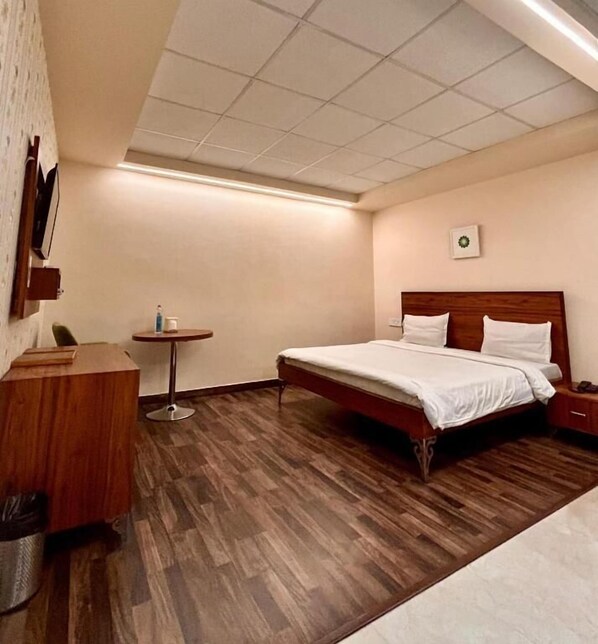 Une chambre d’hôtel avec un lit en bois, une petite table ronde et une poubelle.