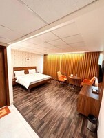 Una habitación de hotel con una cama de madera, un escritorio con silla, una mesita y un televisor.