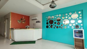 Un hall d’hôtel moderne avec un mur d’accent de couleur turquoise, un comptoir d’accueil et un mur décoratif composé de miroirs.