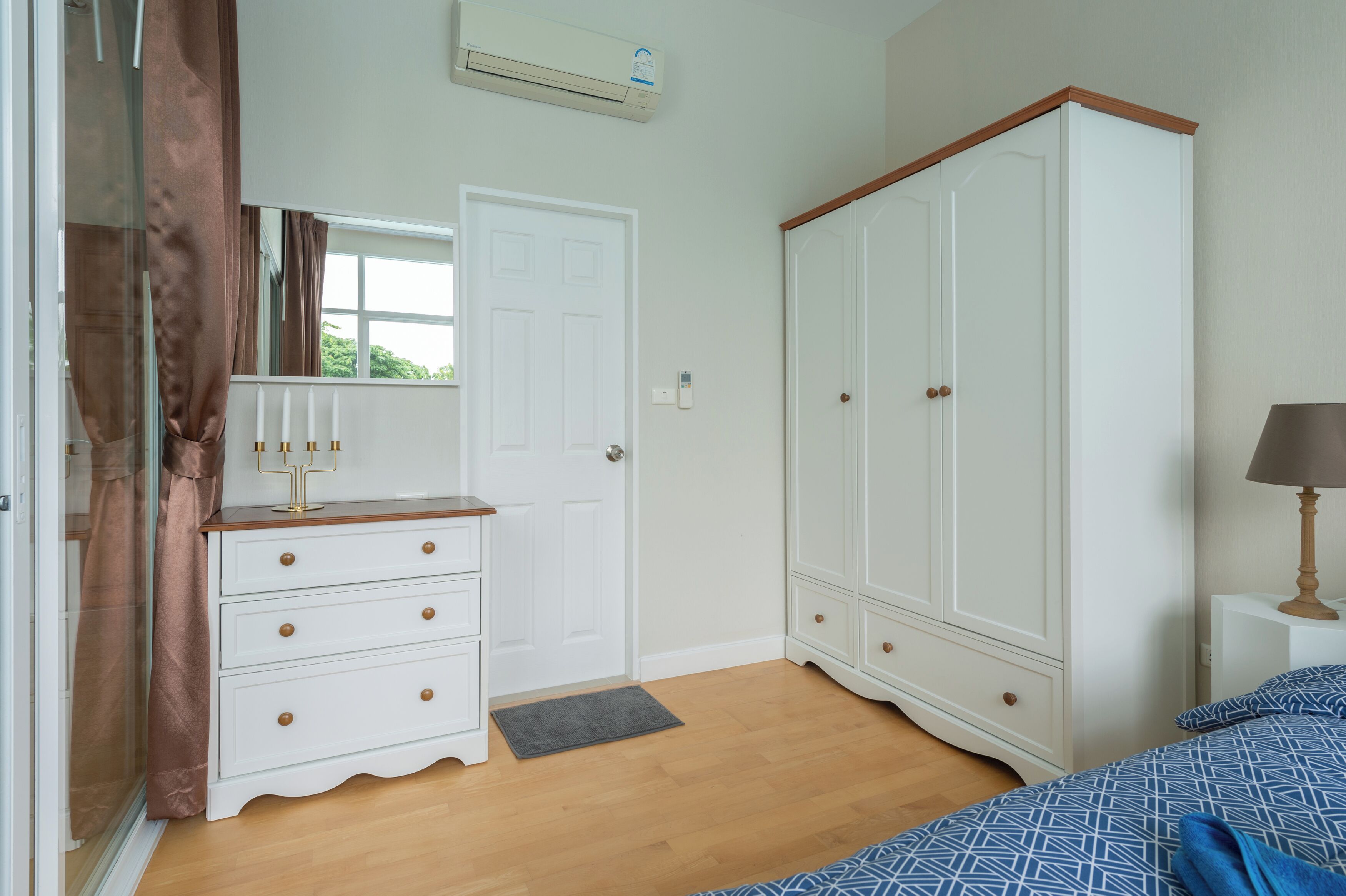 A bedroom with a bed, a dresser, a wardrobe, a mirror, a door, and a window.