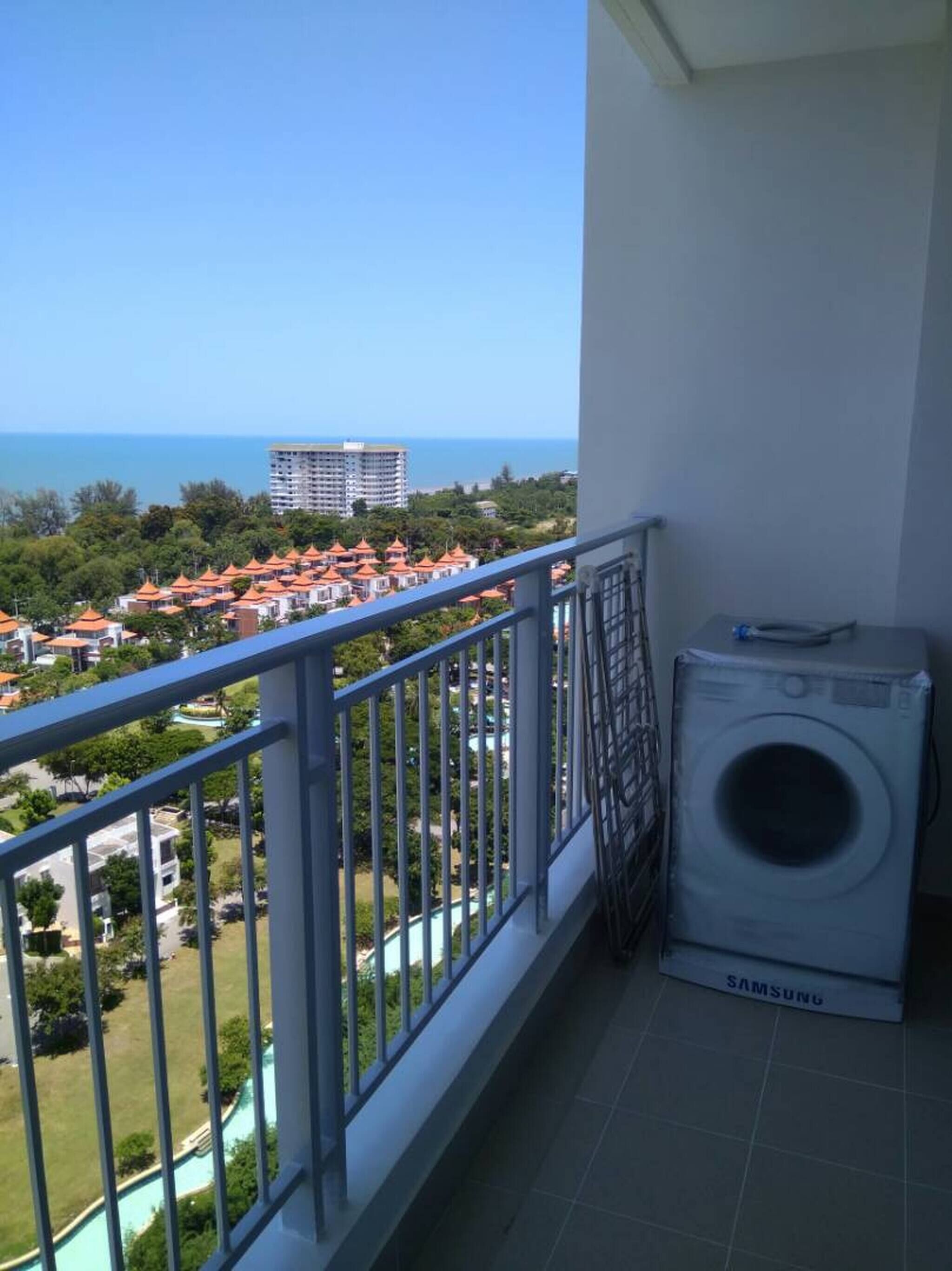 Un balcon avec un lave-linge Samsung, une vue sur une zone côtière avec des bâtiments et une piscine.