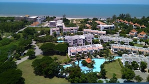 A resort with multiple buildings, a swimming pool, and a beach in the background.