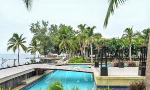 A resort pool with palm trees, a wooden deck, and a view of the sea. - Boathouse Hua Hin Condo (Cha-am)