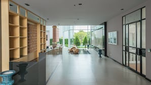 A spacious lobby with a modern design, featuring a reception desk, a large glass window, and a seating area with a water feature.