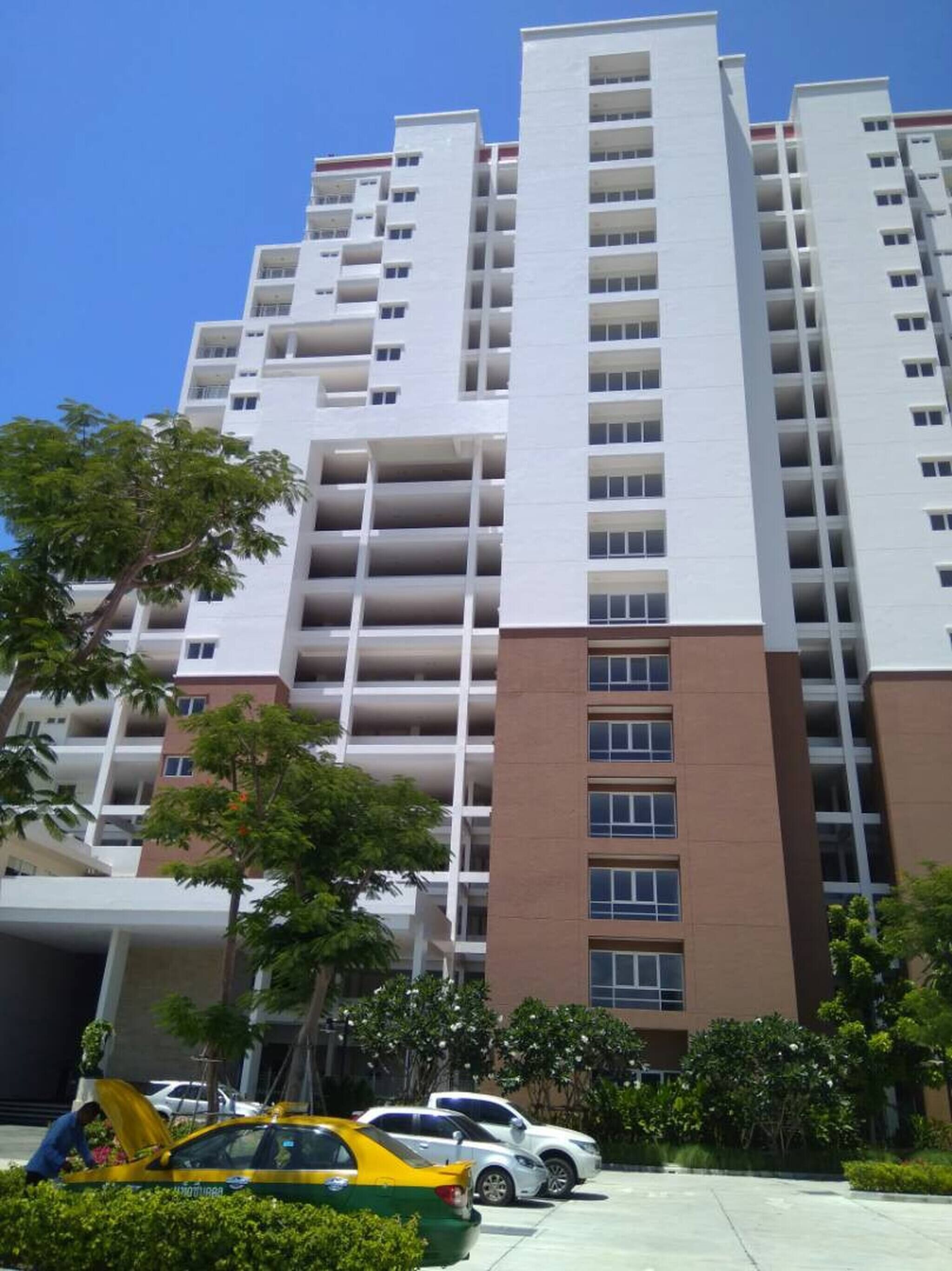 Un immeuble résidentiel à plusieurs étages, doté de balcons, d’un espace de stationnement et de quelques espaces verts.