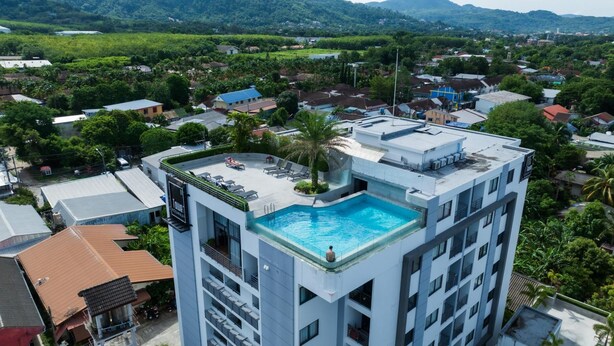 Un hotel di grandi dimensioni con piscina sul tetto, immerso nel verde e con montagne sullo sfondo.