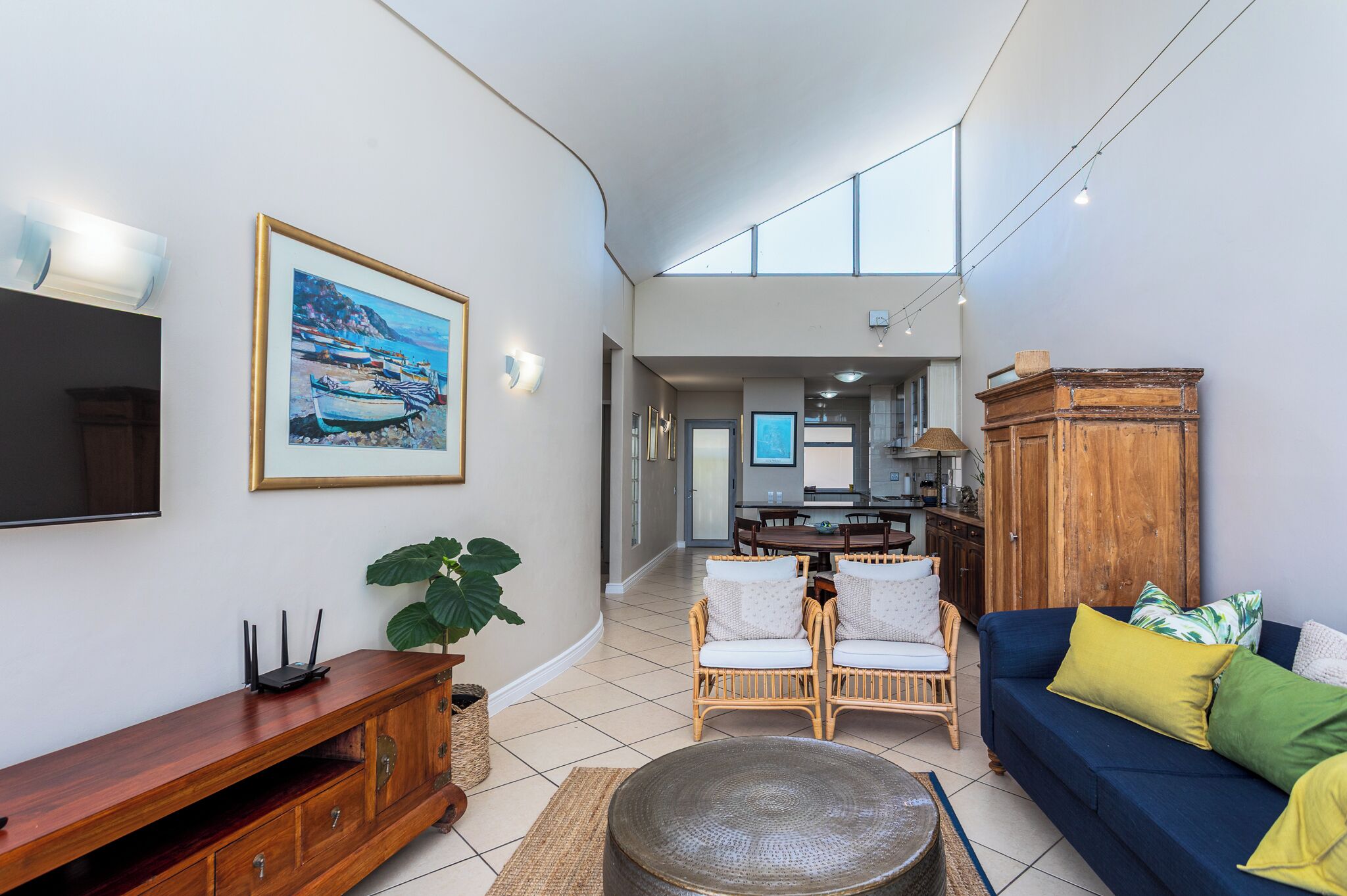 A spacious living area with a dining table, wicker chairs, a blue sofa, and a large painting on the wall.