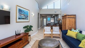 A spacious living area with a dining table, wicker chairs, a blue sofa, and a large painting on the wall. -  Seaside Village C22 by CTHA (Cape Town)