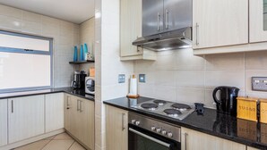 A modern kitchen with light wood cabinets, a stainless steel stove, and a black countertop. -  Seaside Village C22 by CTHA (Cape Town)