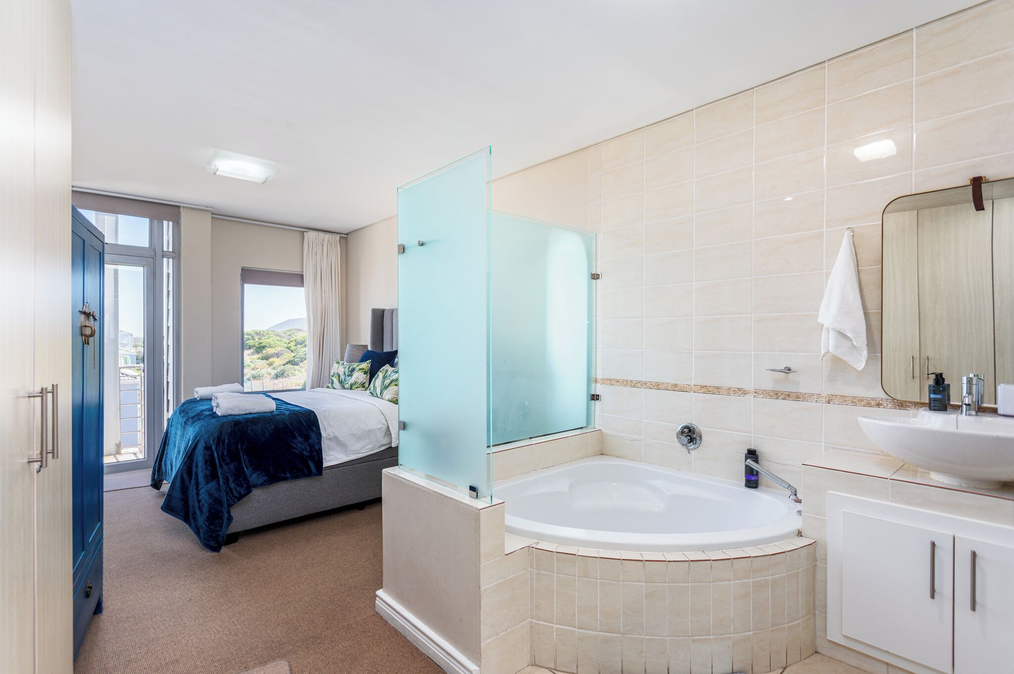 A modern hotel room with a large bed, a glass shower enclosure, a bathtub, and a bathroom with a sink and mirror.