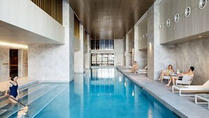 Een modern binnenzwembad met helder water, omringd door ligbedden en een hoog plafond met inbouwverlichting.