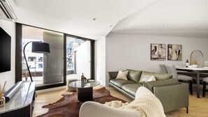 Een moderne zithoek met een leren bank, een glazen salontafel en een eethoek met een witte tafel en stoelen.
