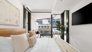Een moderne slaapkamer met een groot bed, uitzicht op de stad door een glazen deur en een tv aan de muur.