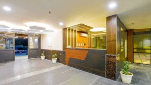 A modern reception area with a wooden reception desk, potted plants, and a glass door entrance. - Aroma Hotel Sultanpur (New Delhi)