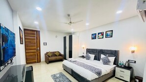 A modern bedroom with a large bed, bedside tables, a TV, and a wooden door. - Aroma Hotel Sultanpur (New Delhi)