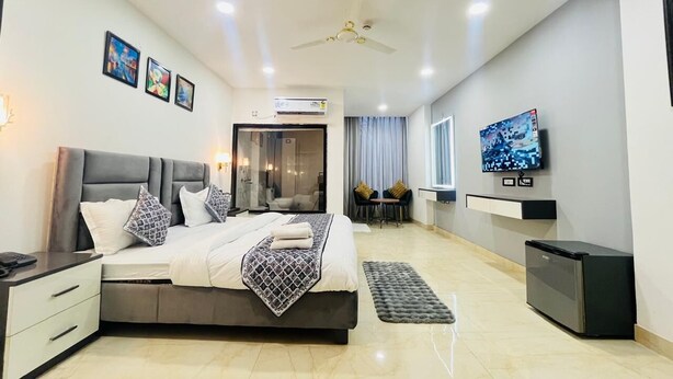 A modern bedroom with a large bed, bedside tables, a TV, and a small fridge. - Aroma Hotel Sultanpur (New Delhi)