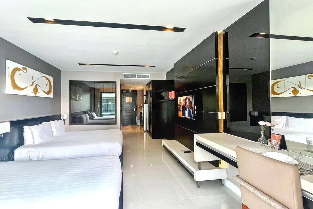 A modern hotel room with a large bed, a TV, a desk, and a seating area.