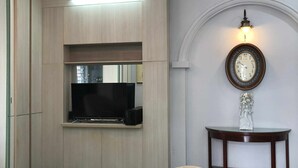 A modern living room with a flat-screen TV, a round wooden table with a clock, and a beige armchair. - The Elegant Comfort Corner in Central District 7, Ho Chi Minh City (P. Tan Phong, Q. 7)