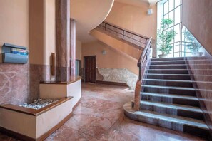 Eine geräumige Lobby mit Marmorboden, einer gewölbten Wand und einer Treppe, die in eine obere Ebene führt.