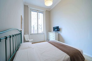 Een slaapkamer met een bed, een stoel, een dressoir en een televisietoestel.
