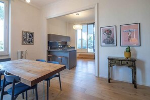 A modern kitchen with a central island, a dining area with a wooden table and blue chairs, and a small side table with a plant.