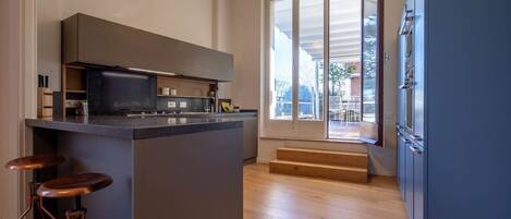 Una cocina moderna con una isla central, taburetes de bar, un ventanal grande y una escalera que conduce a un espacio exterior.