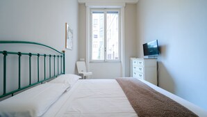 Ein Schlafzimmer mit Bett, Fenster, Stuhl, Kommode und Fernseher.