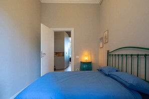 Ein Schlafzimmer mit einem Bett, einem Nachttisch, einer Wandleuchte und einer Tür zu einem anderen Raum.