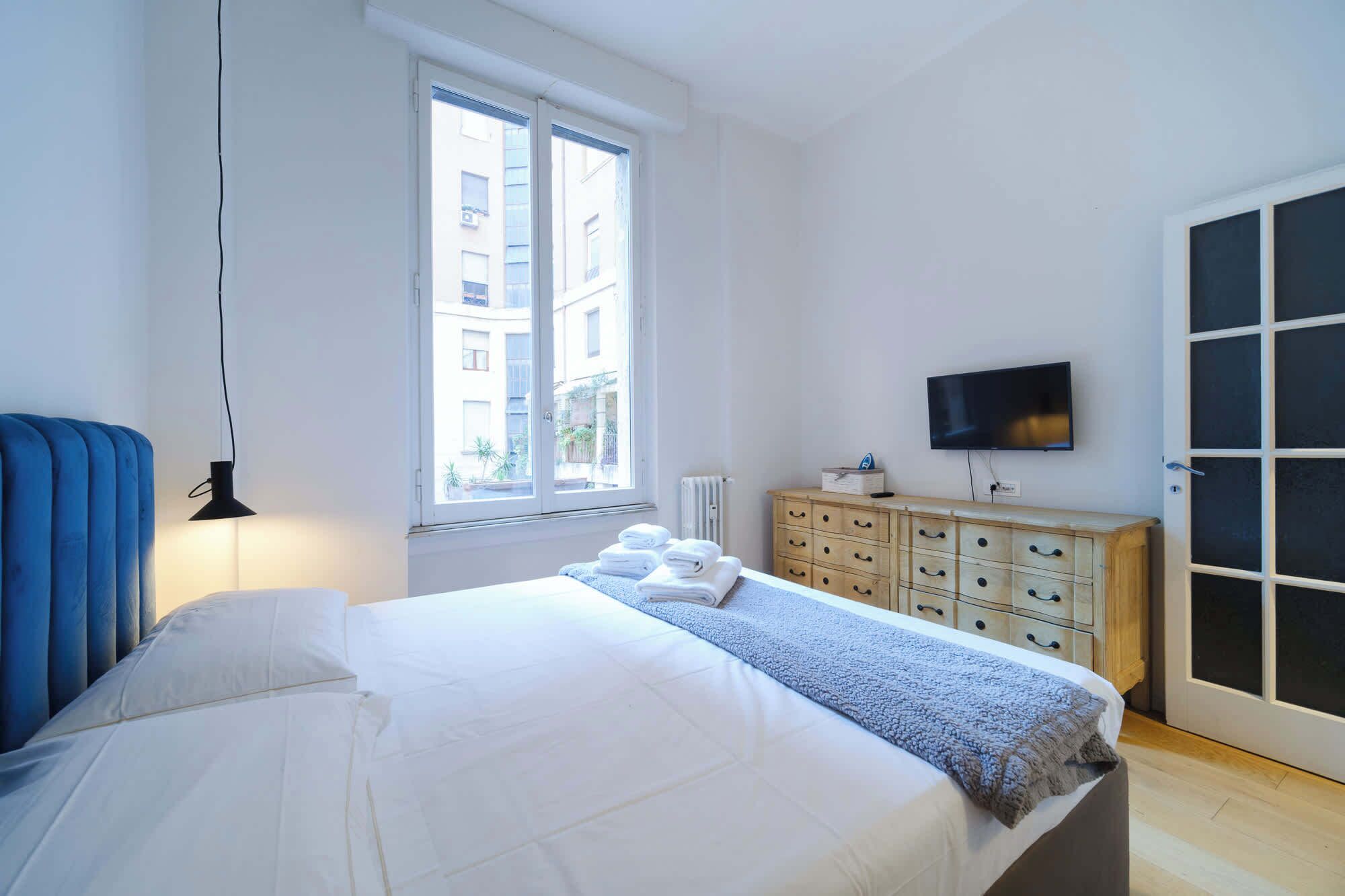 A bedroom with a bed, a dresser, a television, and a window.