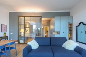 A living room with a sofa, a dining table, chairs, a glass partition, and a wardrobe.