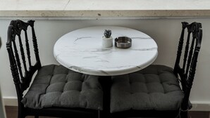 Ett runt bord med en bordsskiva i marmor, två stoppade stolar, en liten krukväxt och en skål i metall på balkongen, med utsikt över en stadsbild med byggnader och träd.