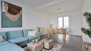 A modern living room with a teal sofa, a coffee table, and a dining area with wicker chairs and a glass table. - Spacious townhouse in the centre of Knokke (Knokke-Heist)