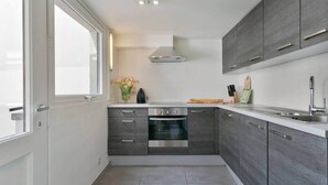 A compact kitchen with a built-in oven, a stainless steel sink, and grey cabinetry. - Spacious townhouse in the centre of Knokke (Knokke-Heist)
