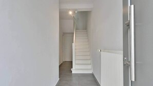 A narrow hallway with a white staircase leading to a door at the end. - Spacious townhouse in the centre of Knokke (Knokke-Heist)