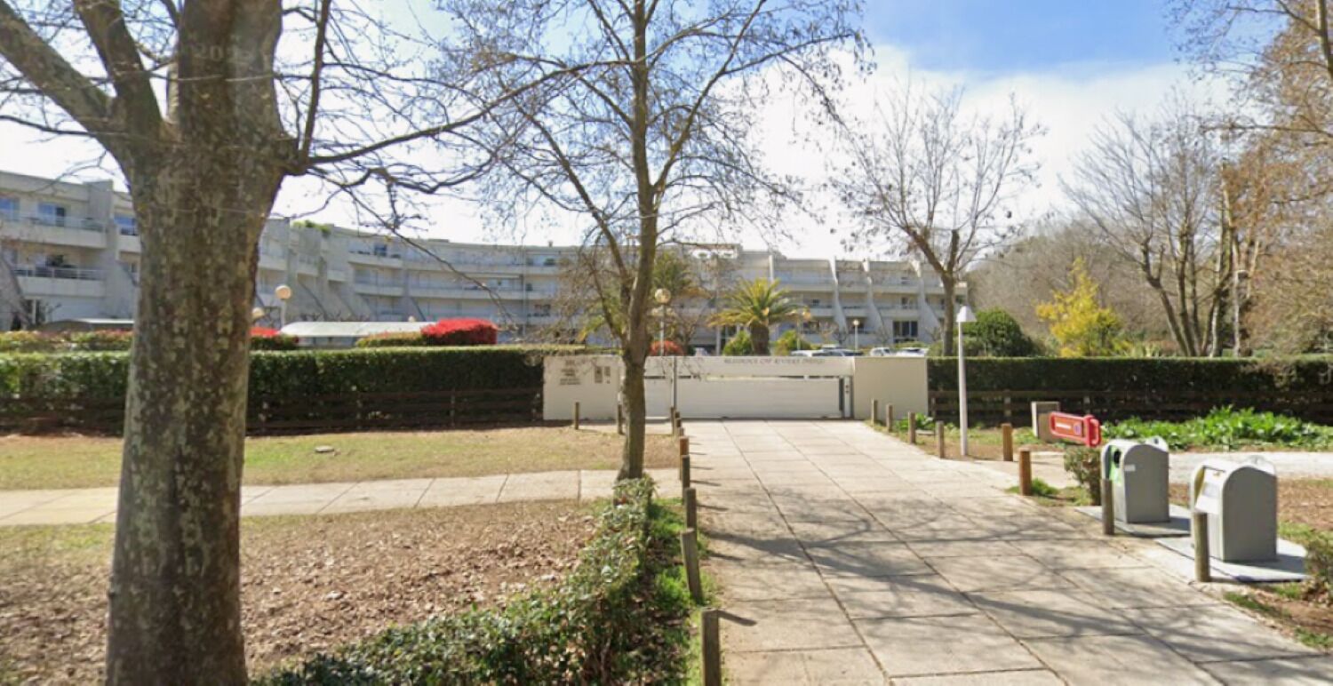 Un chemin menant à un bâtiment doté d’une entrée fermée par un portail, entouré d’arbres et bordé d’une pelouse bien entretenue.