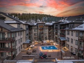 A multi-story hotel with a central courtyard featuring a swimming pool, outdoor seating, and a view of a forested area.